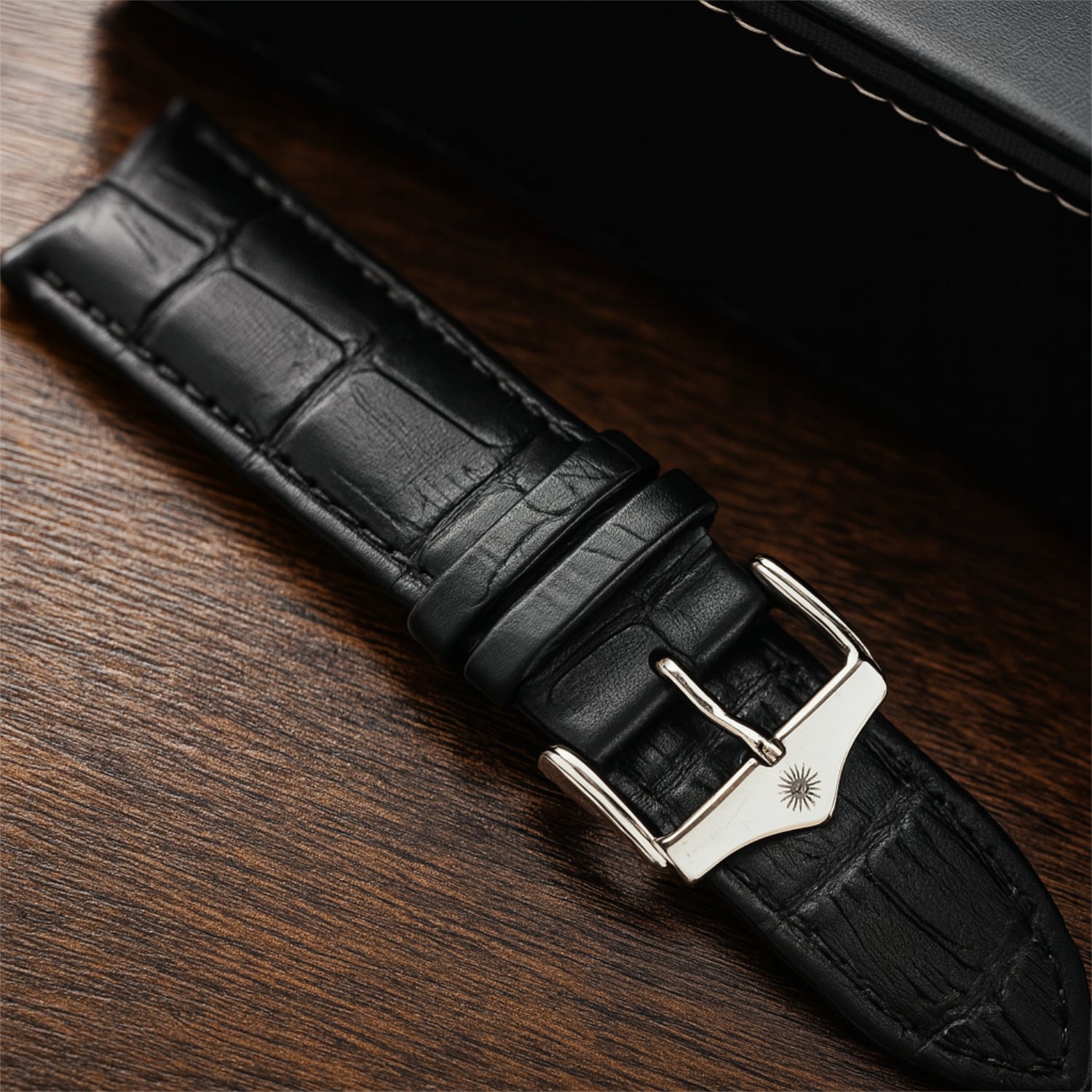 Schwarzes Uhrenarmband aus Leder mit silberner Schnalle auf einem Holztisch.