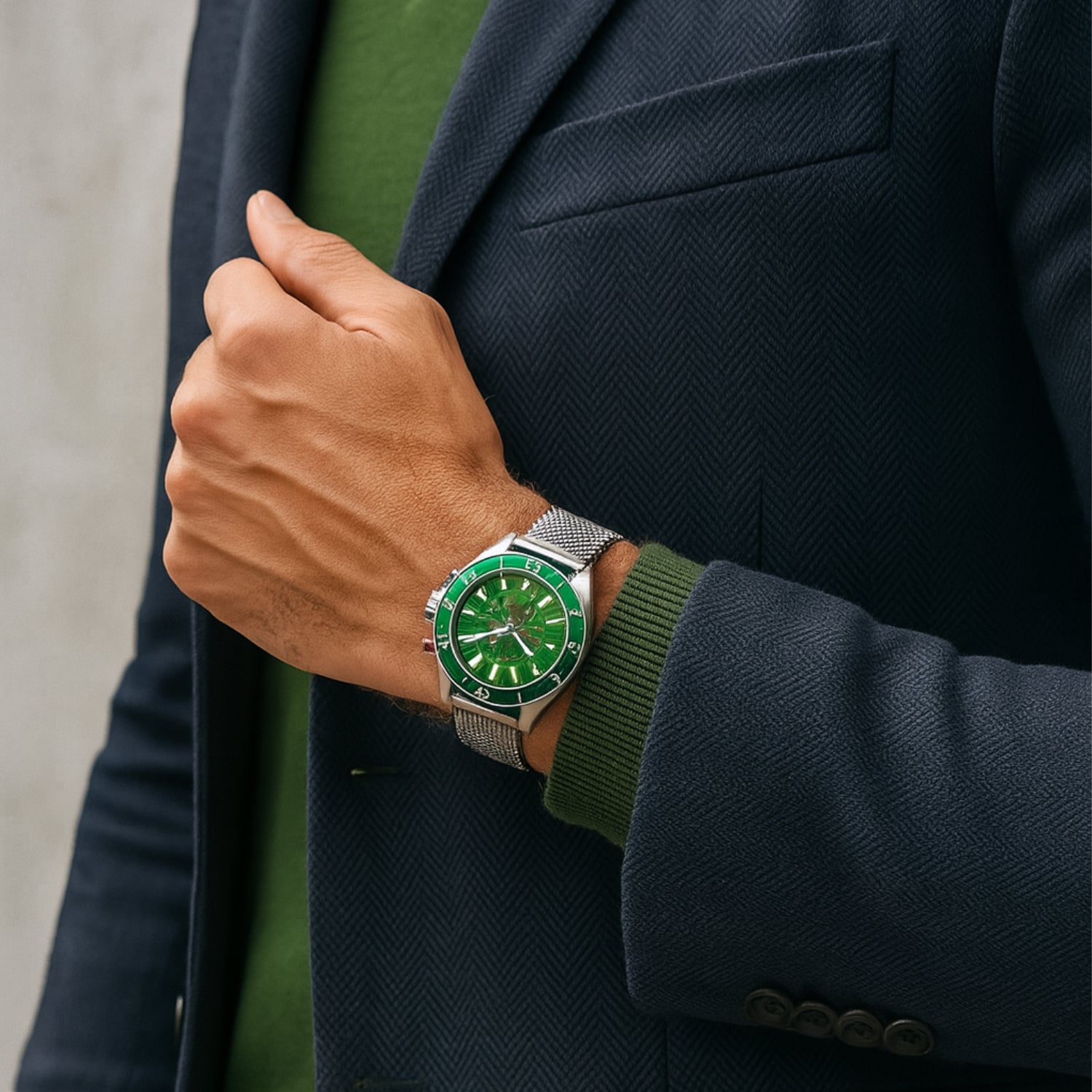 Person im Anzug trägt eine silberne Uhr mit grünem Zifferblatt am Handgelenk.