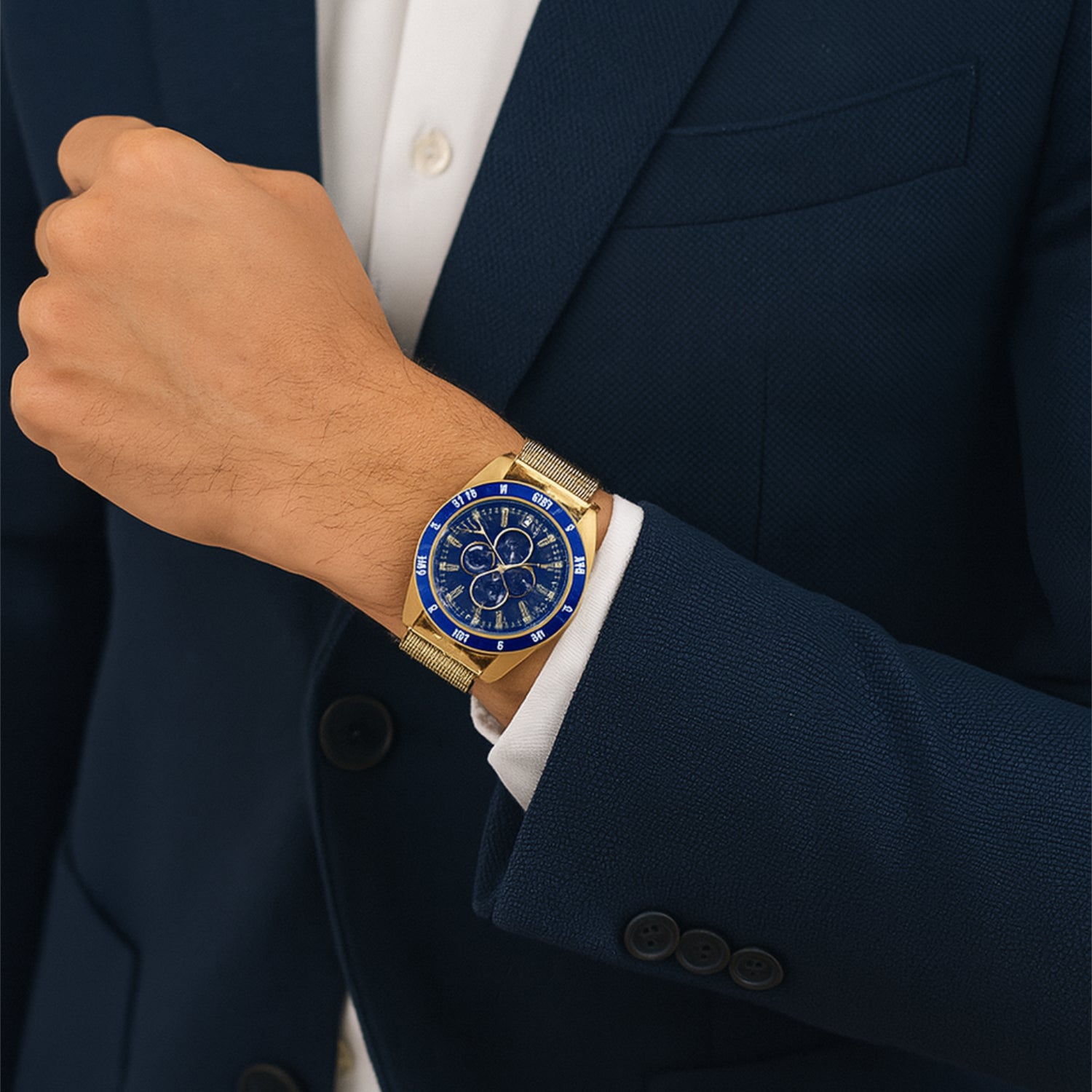 Mann in blauem Anzug trägt am Handgelenk eine goldene Uhr mit blauem Zifferblatt.