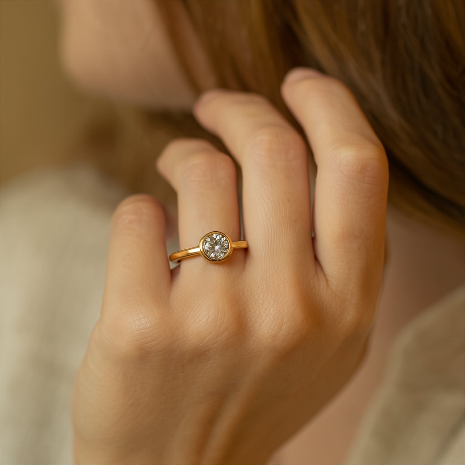 Nahaufnahme einer Hand mit einem goldenen Ring, der einen runden Diamanten trägt.