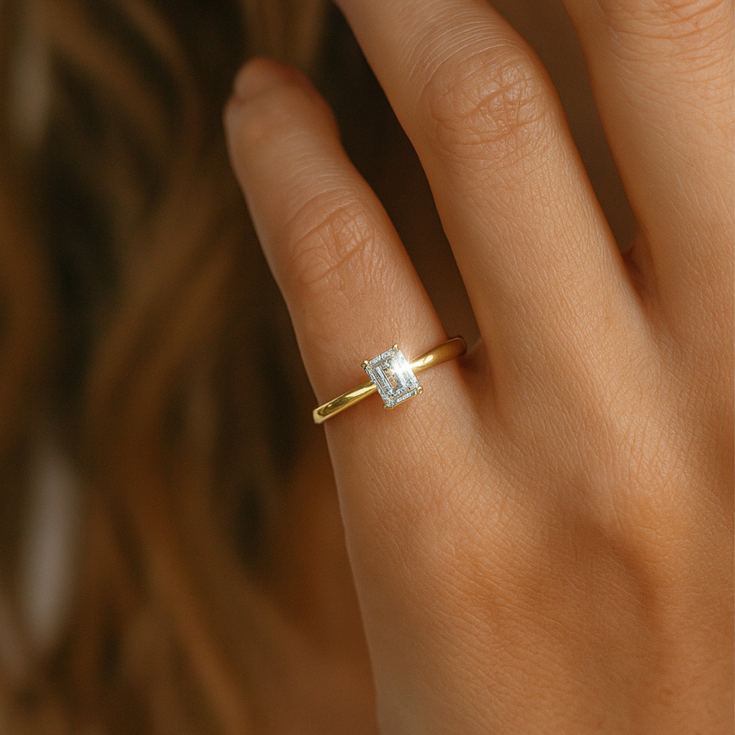 Hand mit goldenem Ring und rechteckigem, funkelndem Edelstein auf einem Finger.