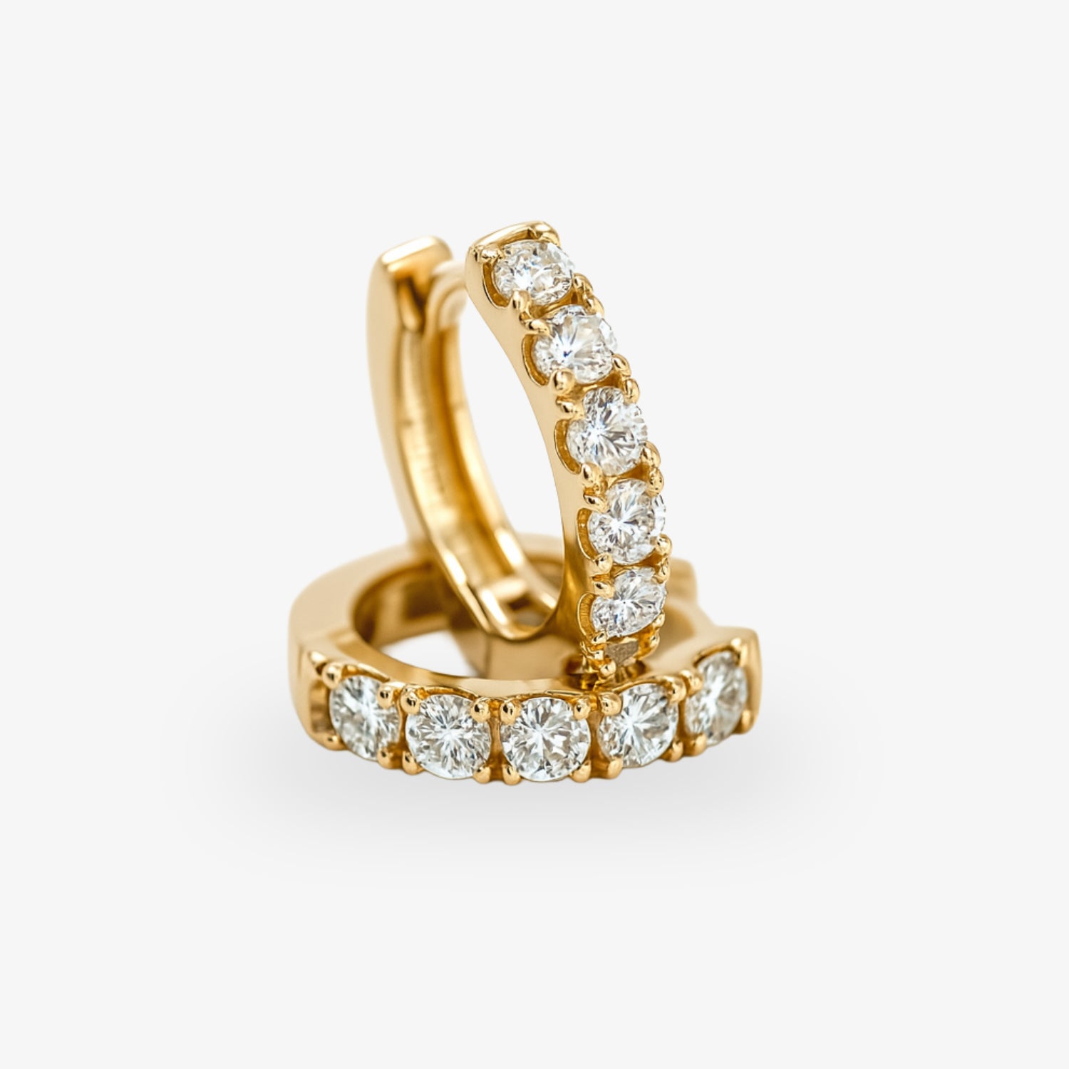 Goldene Creolen mit eingefassten funkelnden Diamanten auf weißem Hintergrund.