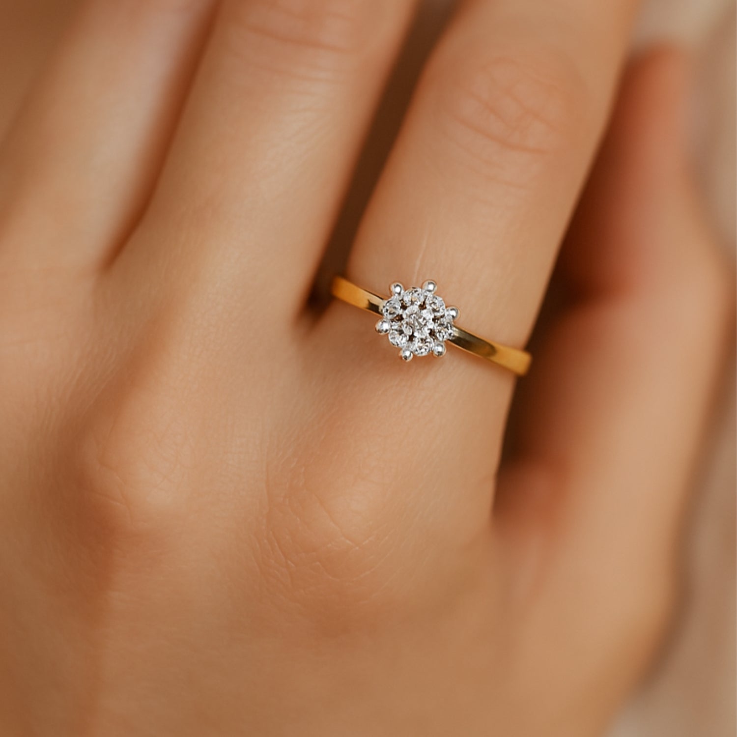 Hand mit einem goldenen Ring, verziert mit einem blumenförmigen Diamantencluster.