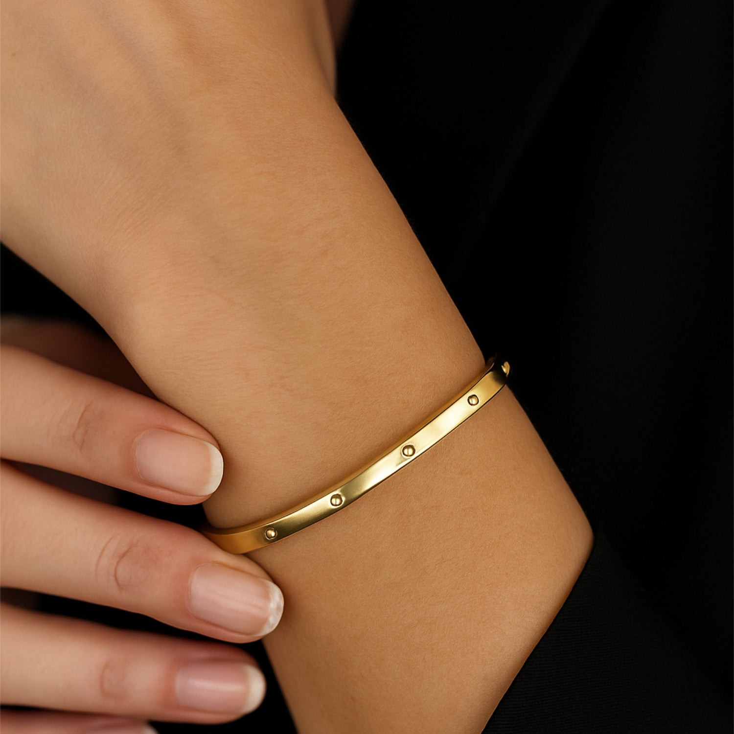 Nahaufnahme eines goldenen Armreifs am Handgelenk einer Person auf schwarzem Hintergrund.