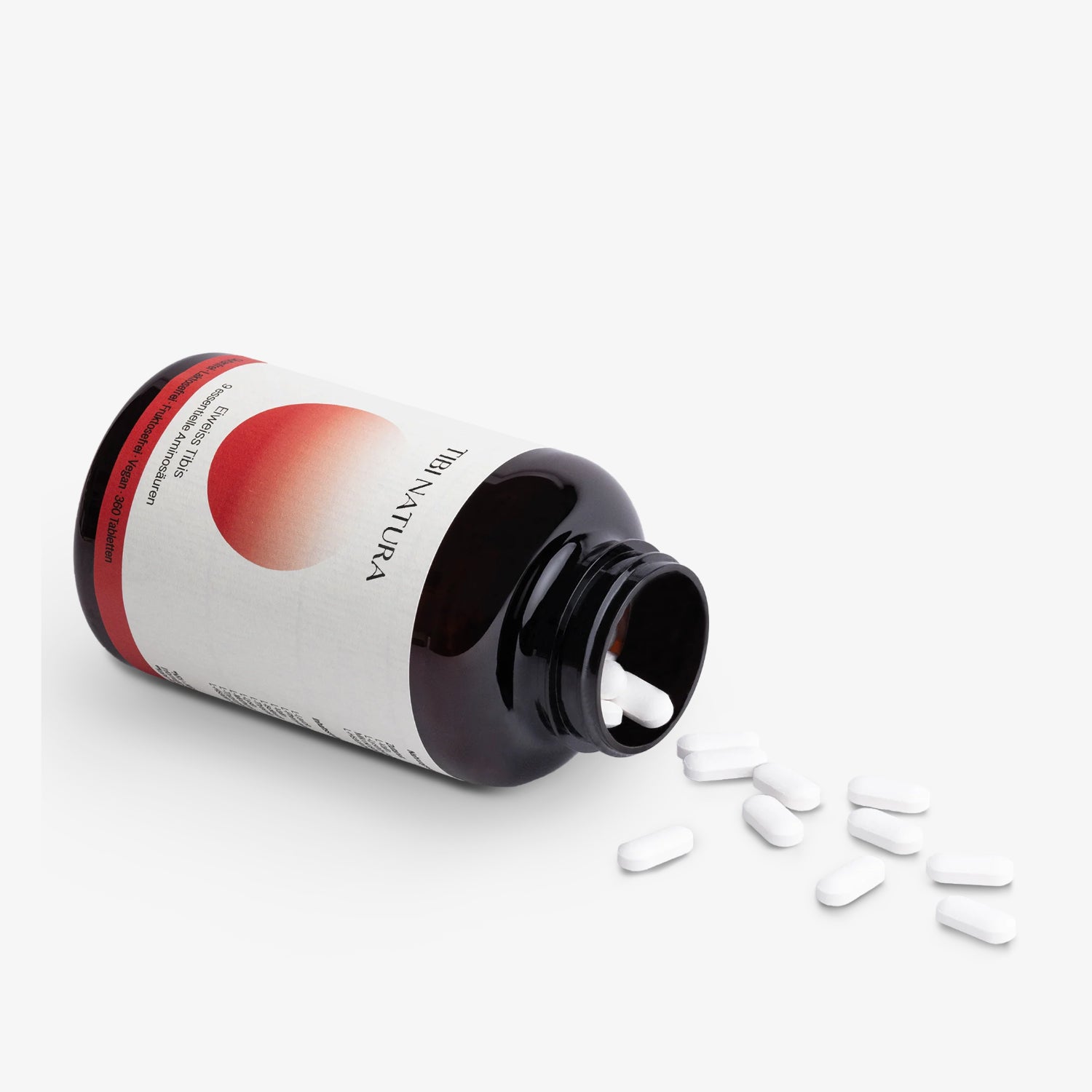 Braune Flasche mit der Aufschrift "Ibi Natura", aus der weiße Tabletten auf einen weißen Hintergrund fallen.