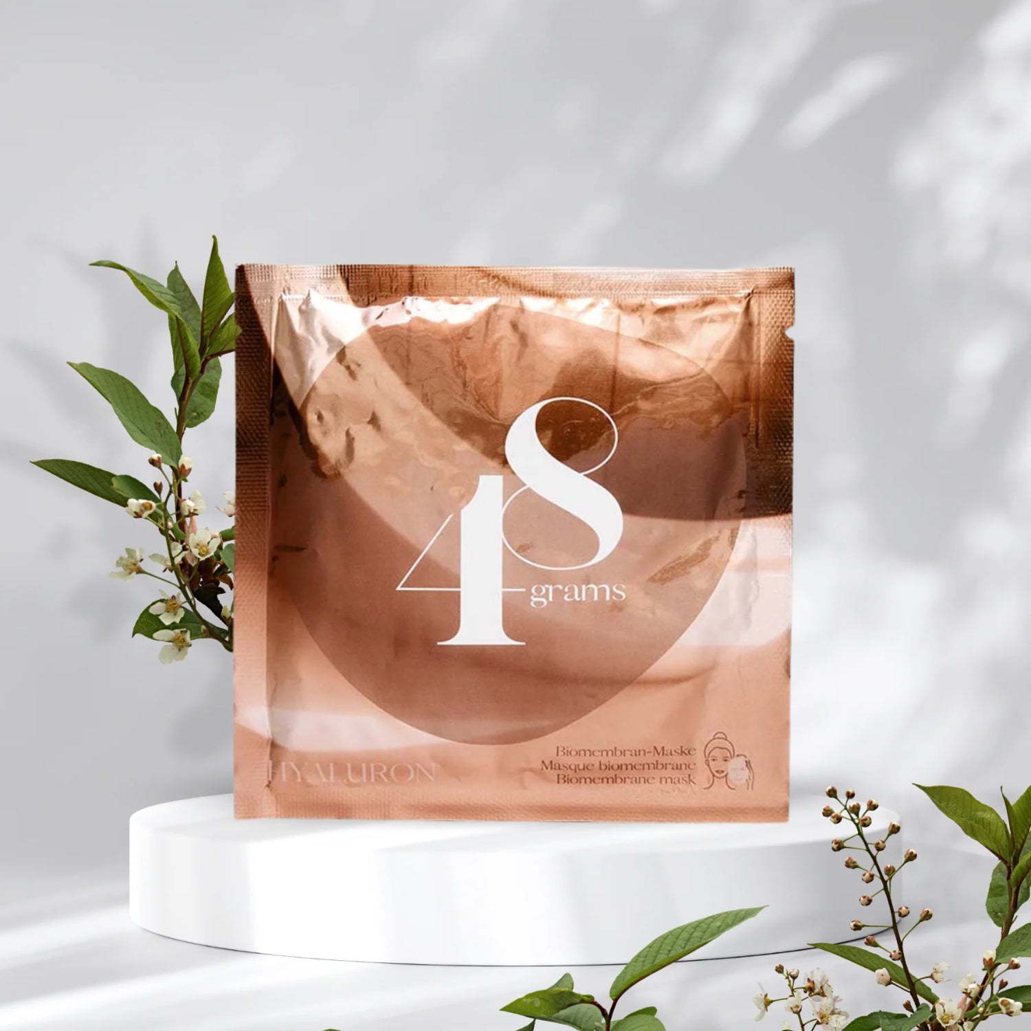 Kupferfarbene Verpackung mit der Aufschrift "48 grams", umgeben von grünen Zweigen auf weißem Hintergrund.