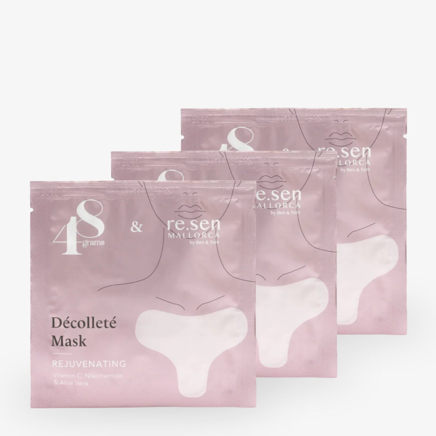 Drei rosa Verpackungen von Dekolleté-Masken mit Vitamin C, Niacinamid und Aloe Vera auf hellem Hintergrund.