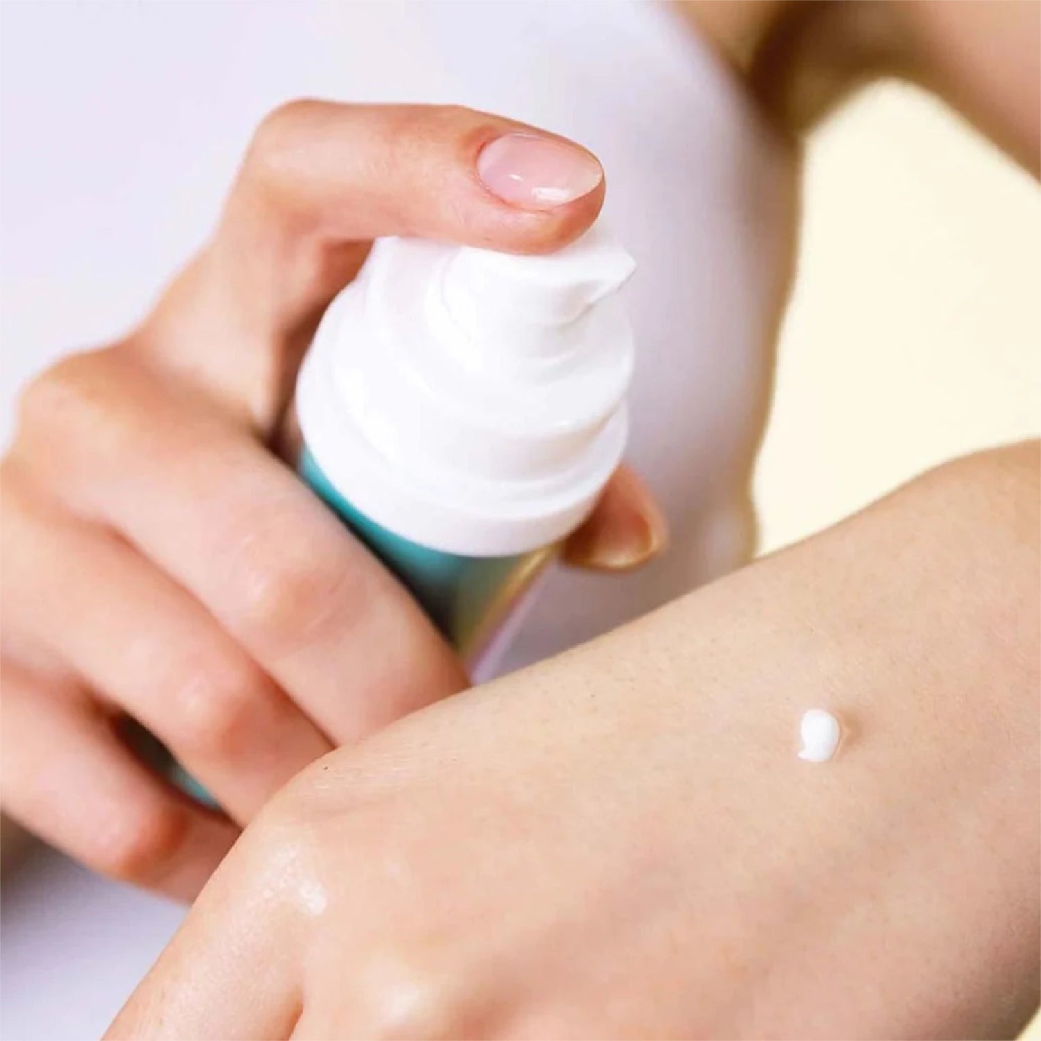 Hand trägt weißen Schaum aus einer Dose auf Haut auf.