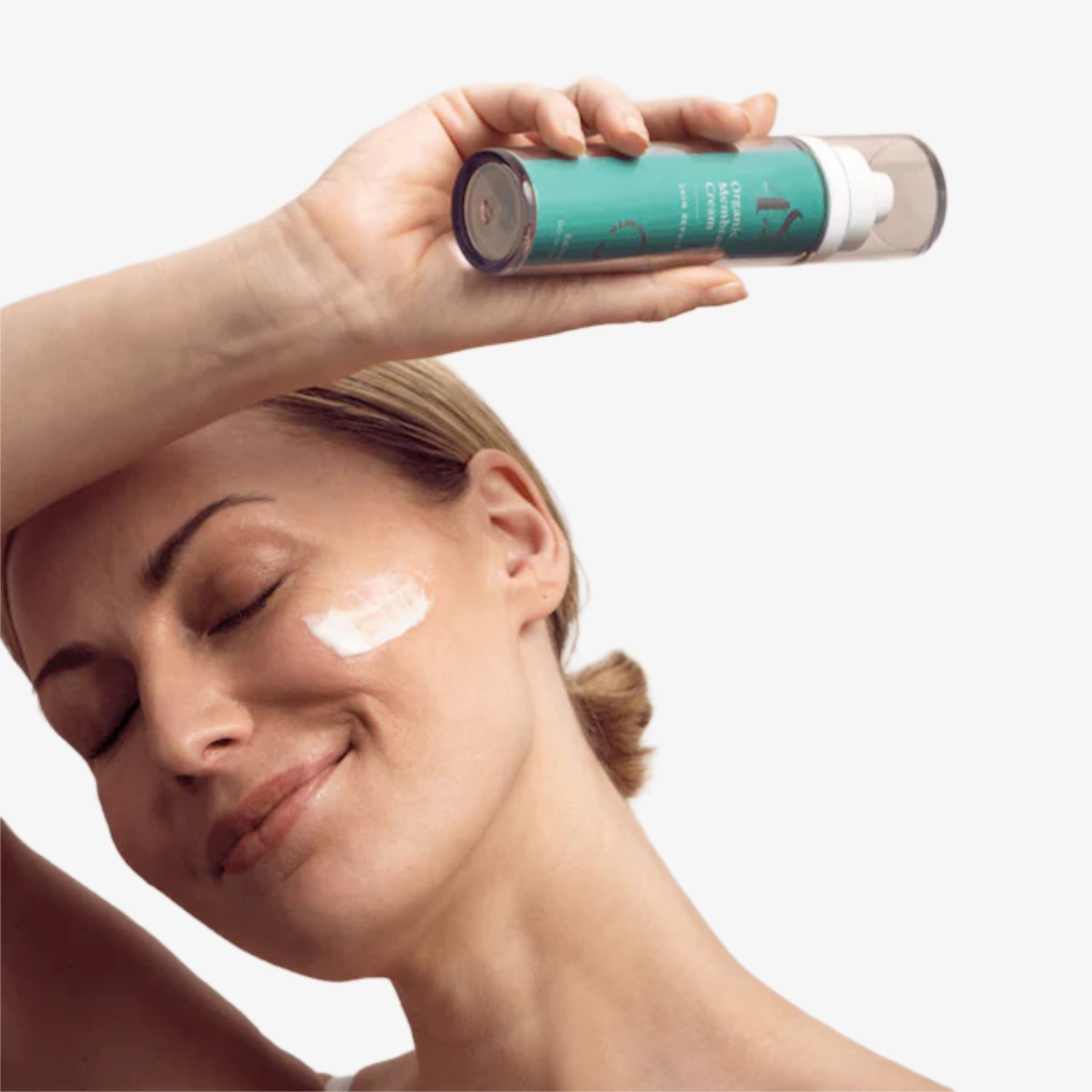 Frau trägt Feuchtigkeitscreme auf die Wange auf und hält eine grünes Produktfläschchen in der Hand.