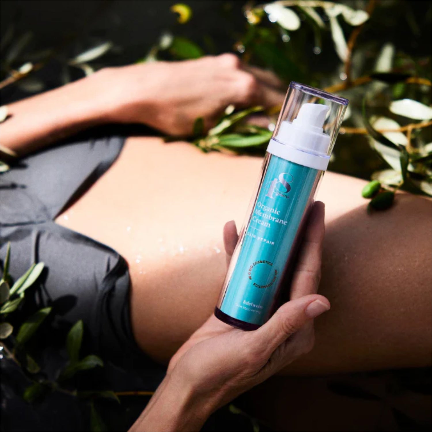 Person hält eine Flasche mit Hautcreme neben einem Bauch, umgeben von grünen Blättern.