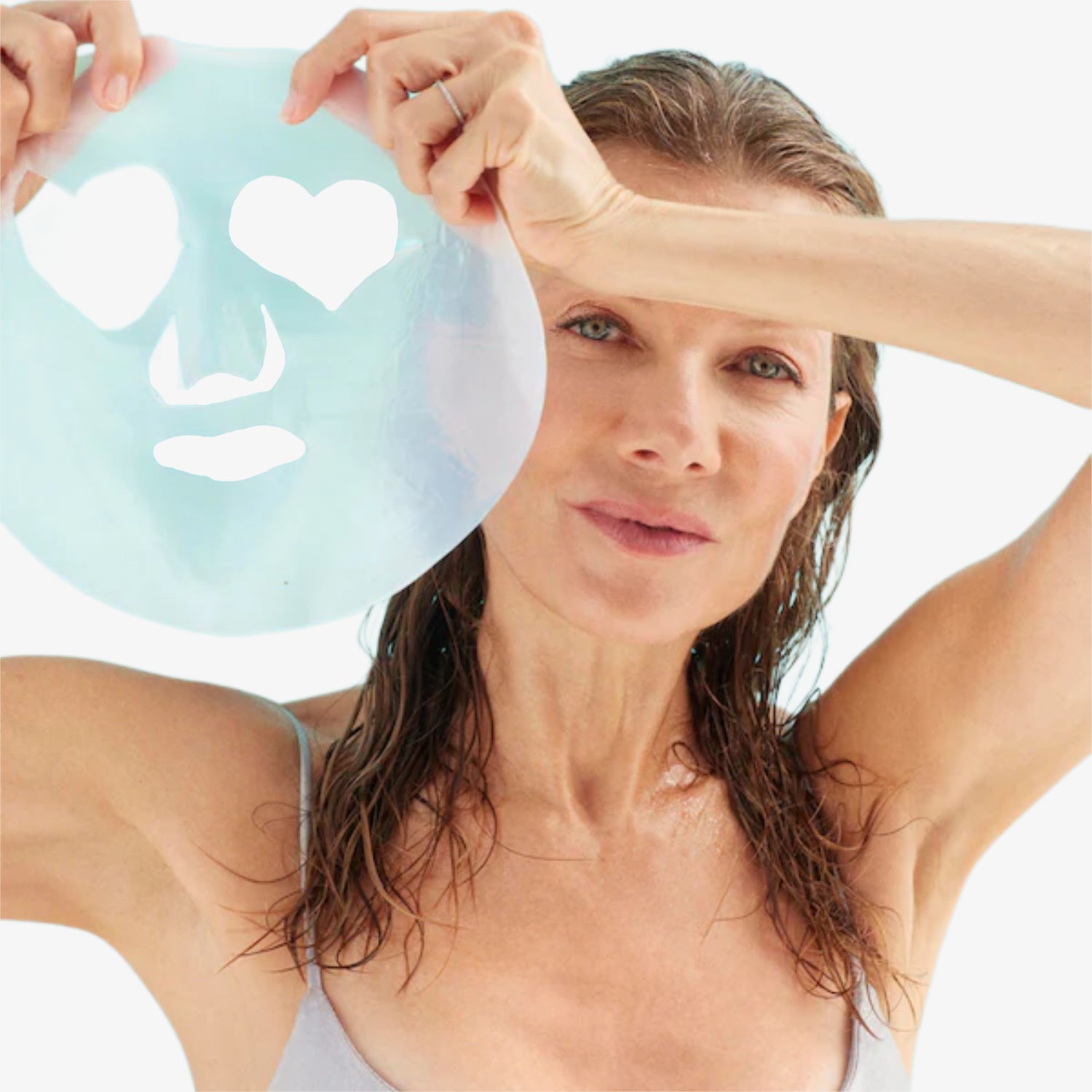 Frau hält eine Gesichtsmaske mit Herzformen über ihrem Gesicht, während sie leicht lächelt.