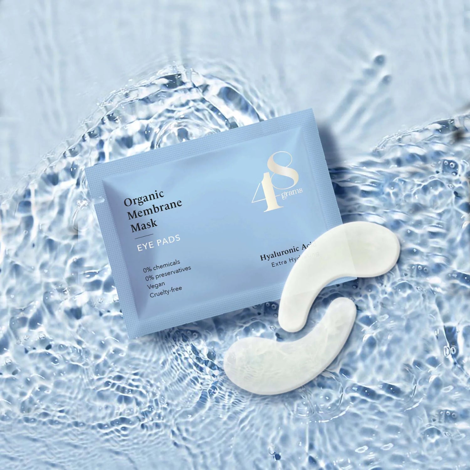 Blaue Verpackung von Augenpads auf Wasseroberfläche, daneben zwei weiße Gel-Pads.