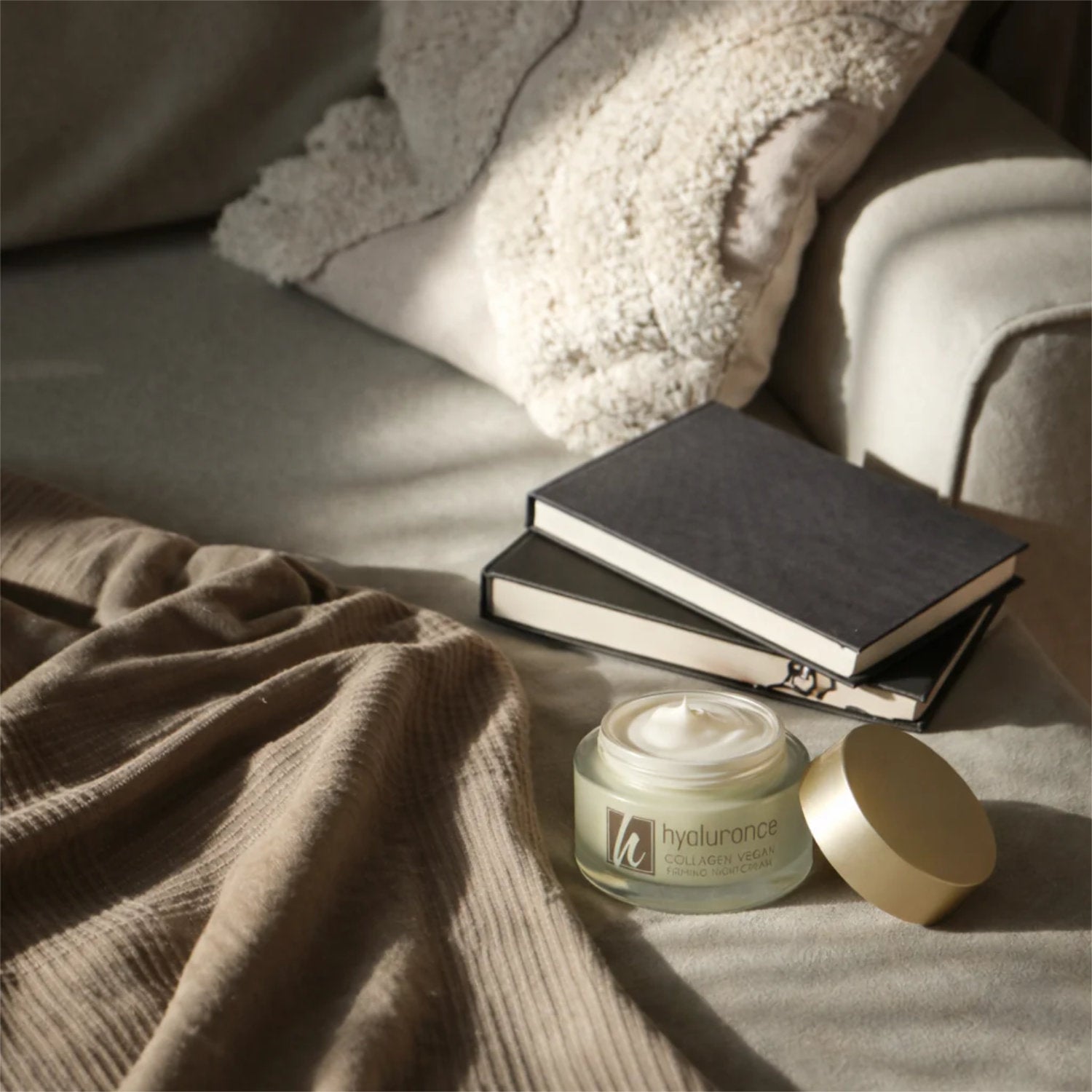 Nachtcreme von hyaluronce auf einem Sofa mit Notizbüchern und Decke, ideal für nächtliche Hautpflege.