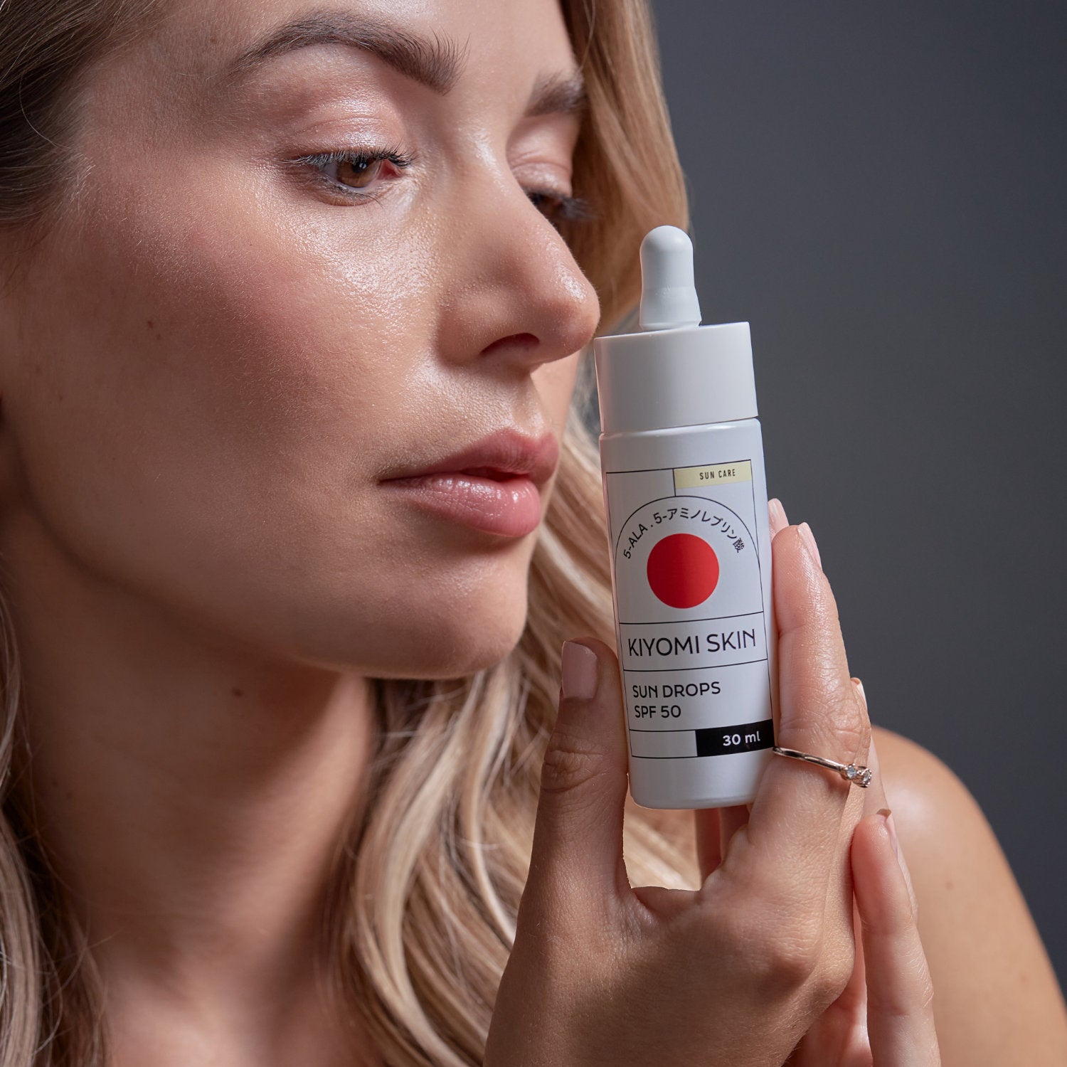 Frau hält das Sonnenserum Sun Drops SPF 50 von Kiyomi Skin in der Hand, ideal für empfindliche Haut.