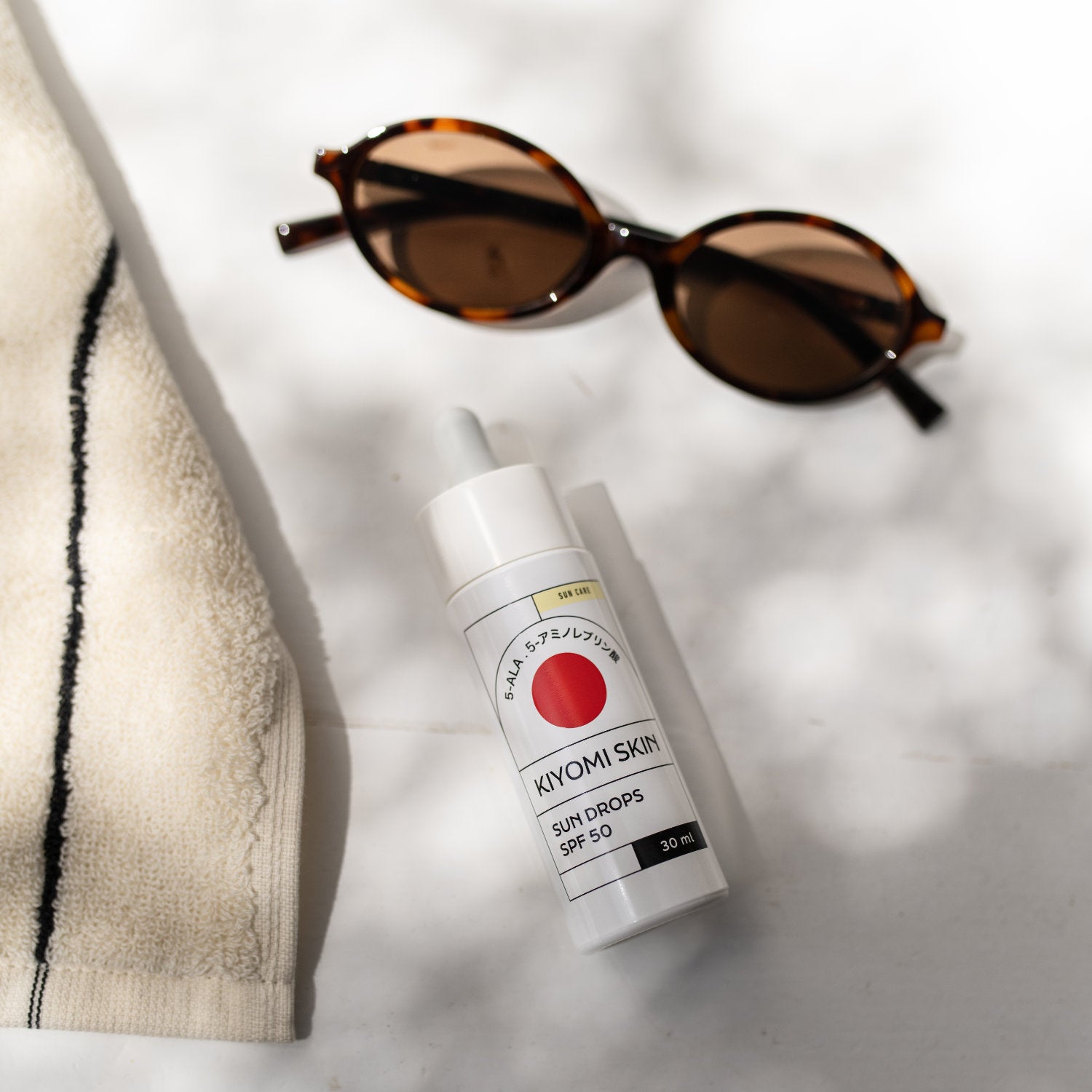 Sun Drops SPF 50 Sonnenserum für Gesicht, 30 ml, mit Sonnenbrille und Handtuch im Hintergrund.