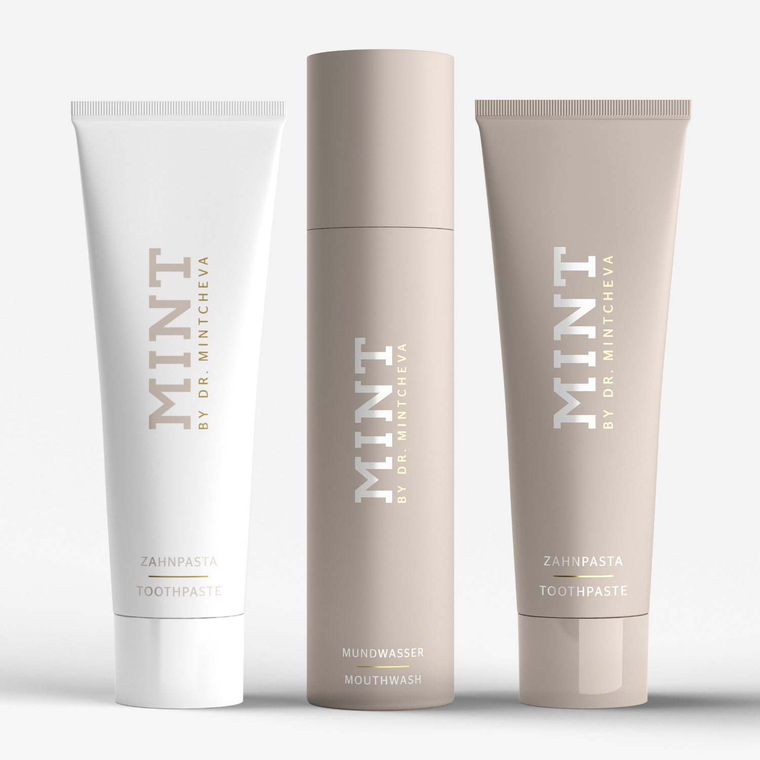 Drei Produktflaschen von "MINT" mit Zahnpasta und Mundwasser in schlichten, eleganten Verpackungen vor weißem Hintergrund.