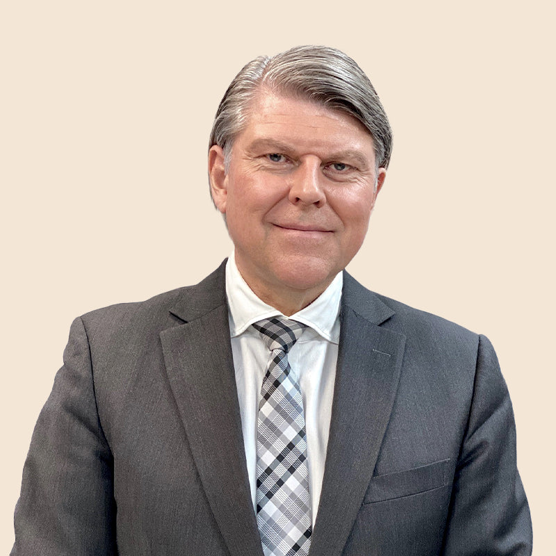 Mann in grauem Anzug und karierter Krawatte vor beigem Hintergrund.
