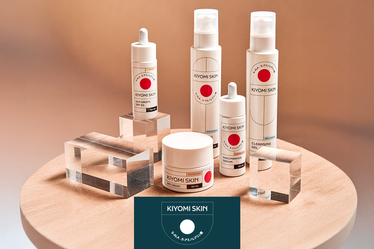 Mehrere Kiyomi Skin Pflegeprodukte stehen auf einem runden Holztisch, umgeben von transparenten Blöcken.