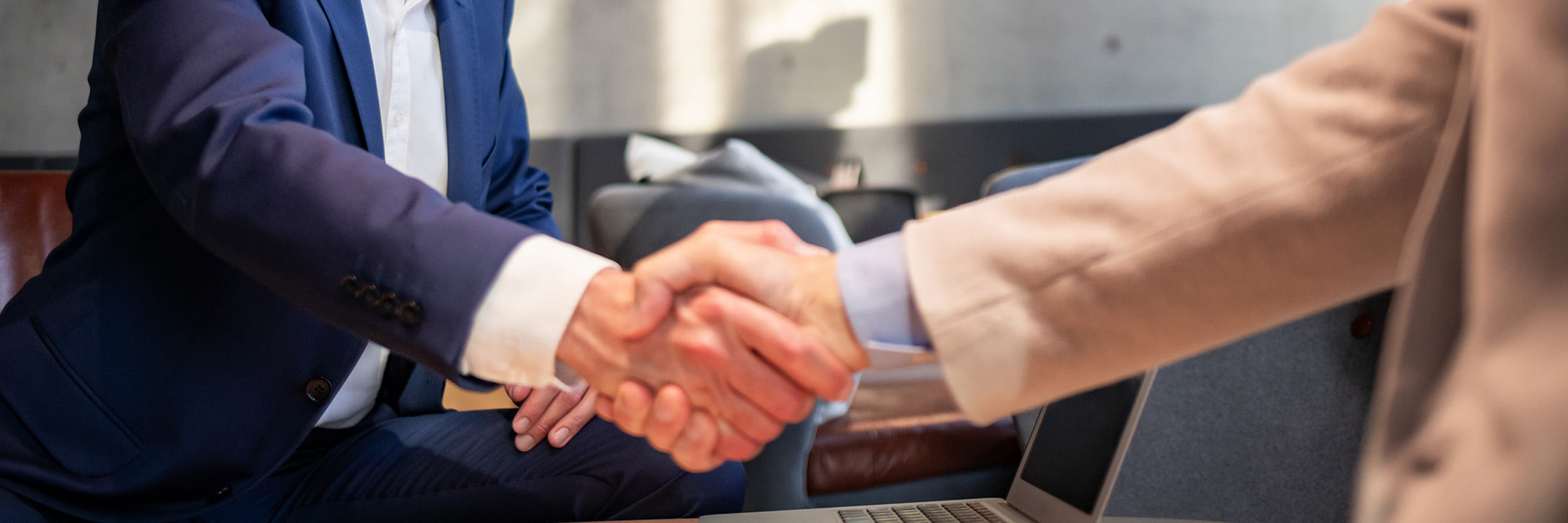 Zwei Personen schütteln sich die Hände über einem Tisch mit einem Laptop.