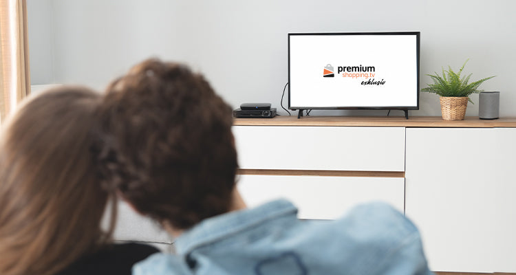 Paar sitzt auf einem Sofa und schaut auf einen Fernseher, der das "Premium Shopping TV" Logo zeigt.