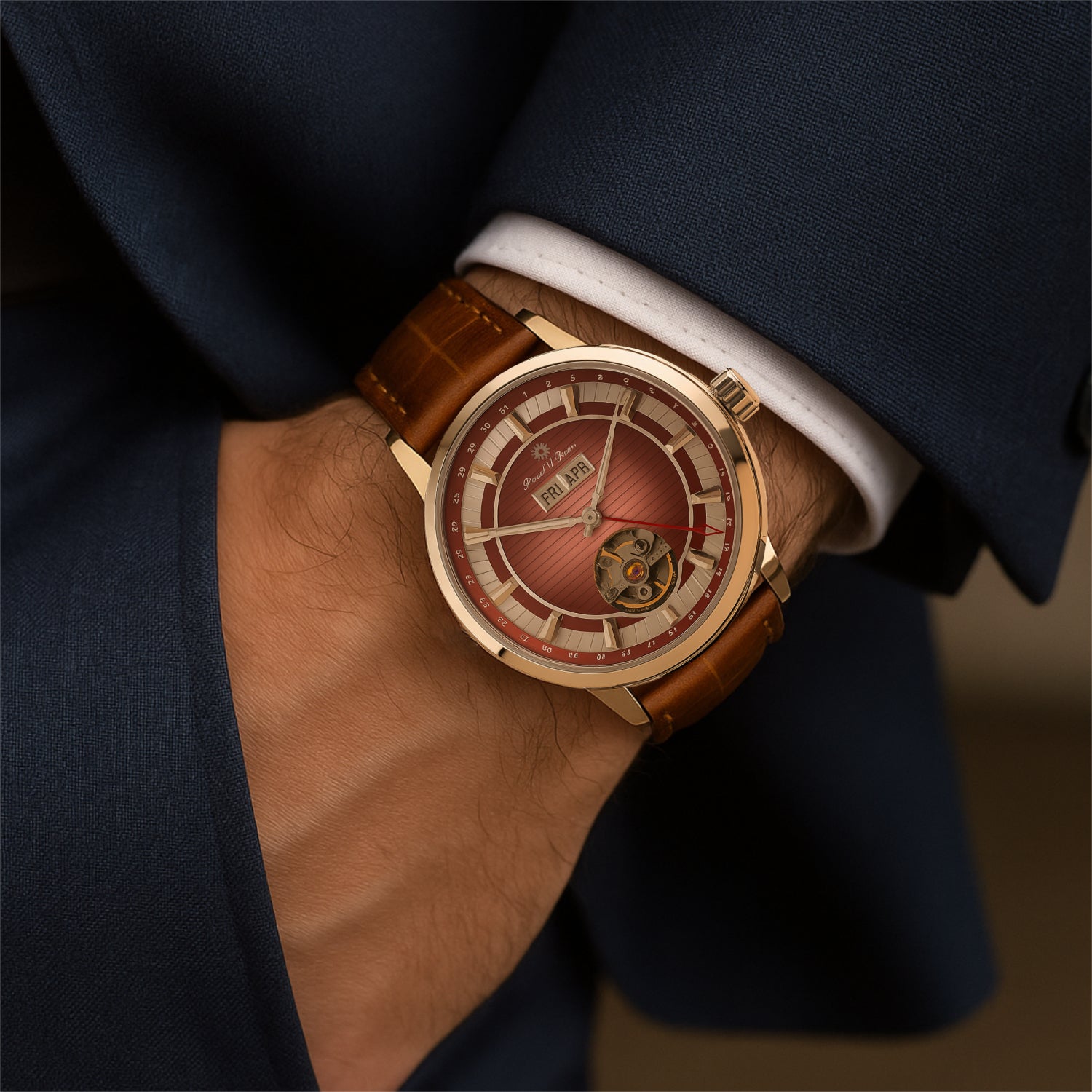 Person in einem dunkelblauen Anzug trägt eine Uhr mit roségoldenem Gehäuse, rötlichem Zifferblatt und braunem Armband.