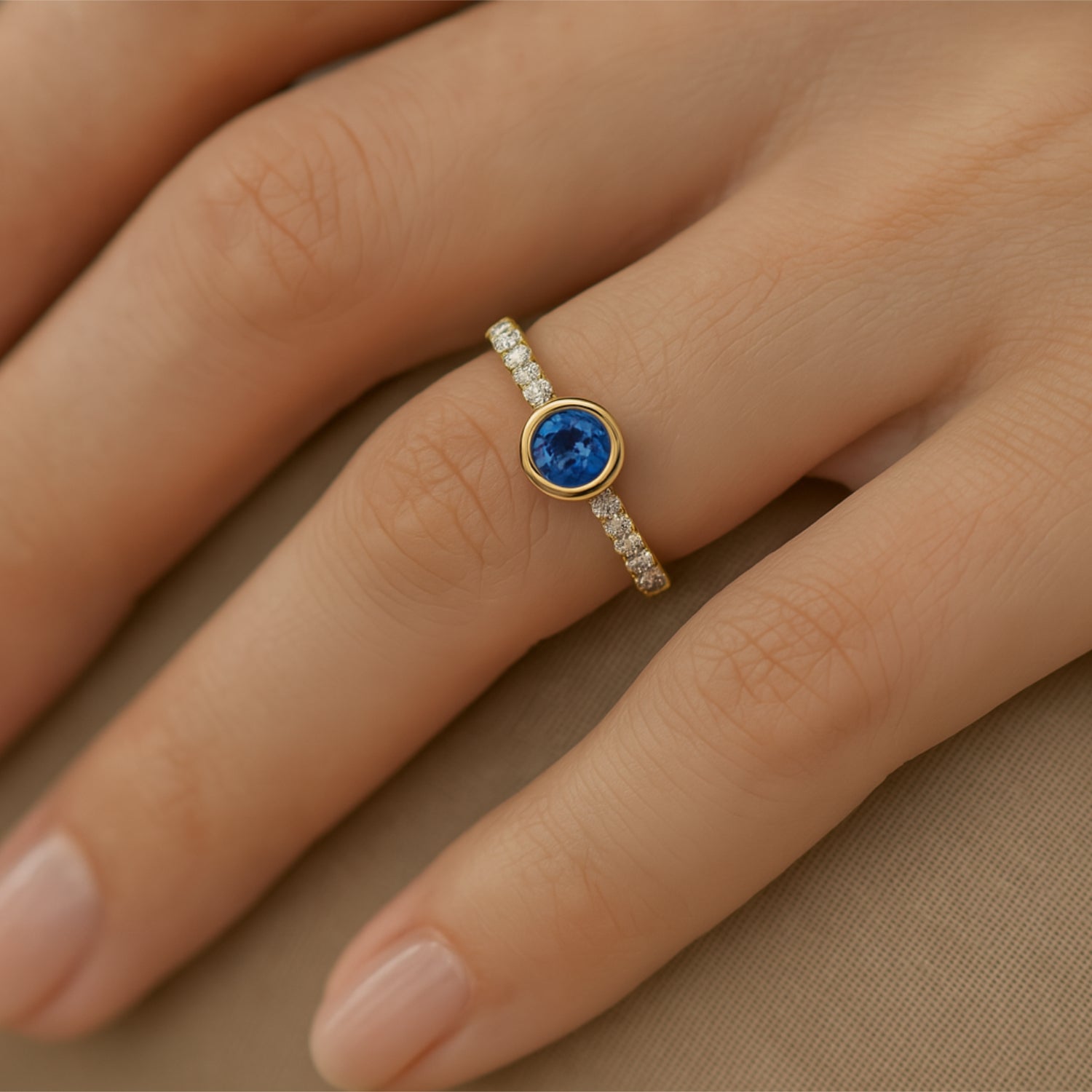 Hand mit Ring, der einen blauen Edelstein in einer goldenen Fassung und funkelnde Diamanten auf dem Band zeigt.