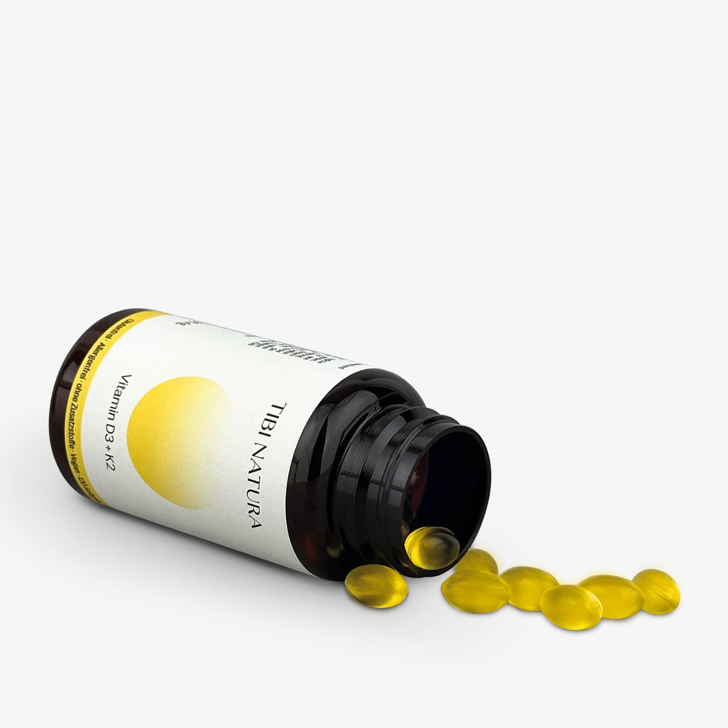 Braunes Glasfläschchen mit gelben Vitaminkapseln, liegend mit herausfallenden Kapseln.