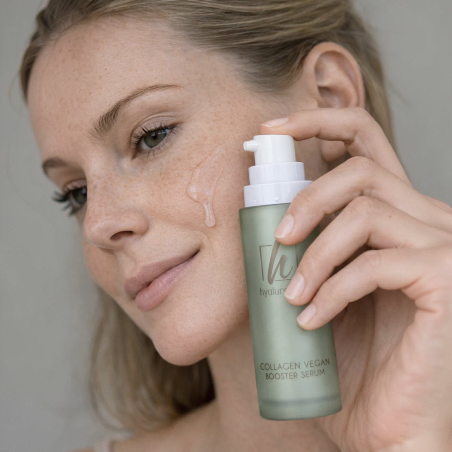 Frau trägt hyaluronce Collagen Vegan Booster Serum auf ihr Gesicht auf, um ihre Haut zu revitalisieren.