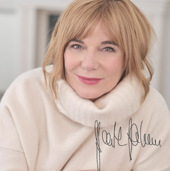 Frau mit blonden Haaren in cremefarbenem Rollkragenpullover lächelt in die Kamera, mit Unterschrift im Bild.