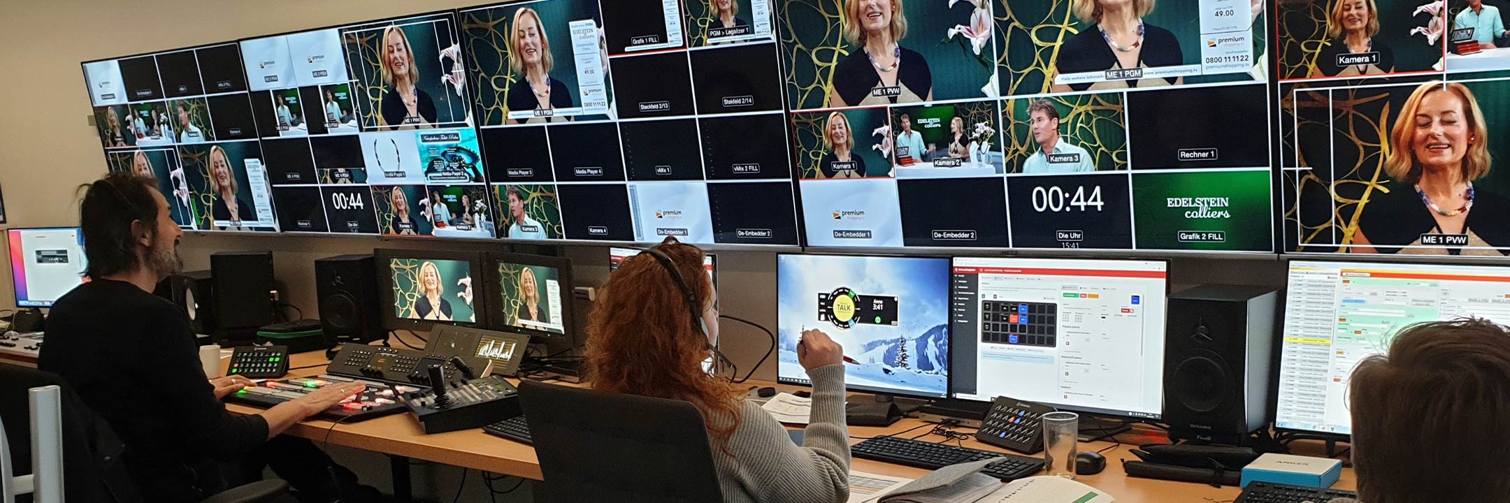 Personen arbeiten in einem Kontrollraum mit vielen Bildschirmen, die ein Fernsehprogramm überwachen.