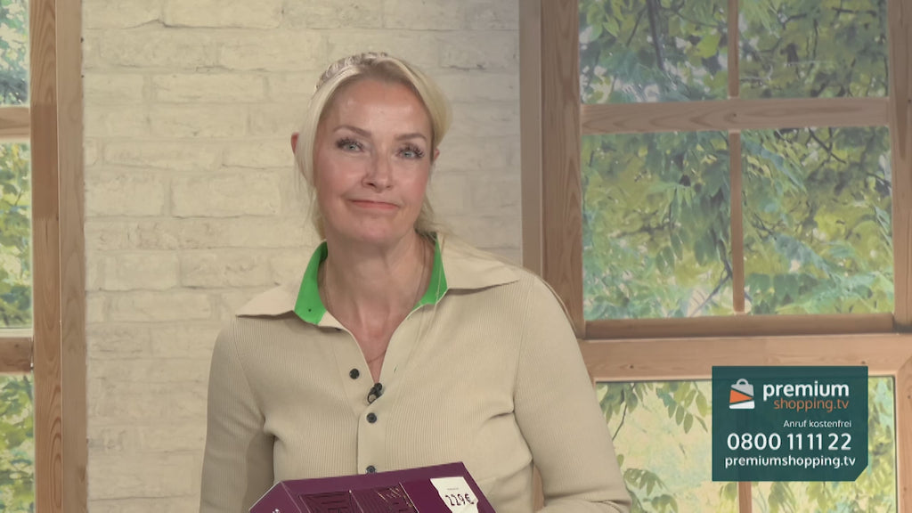 Video-Vorschaubild: Blonde Moderatorin hält eine burgunderfarbene Produktbox mit Preisschild vor einer Backsteinwand, unten rechts das premiumshopping.tv-Logo mit Telefonnummer.