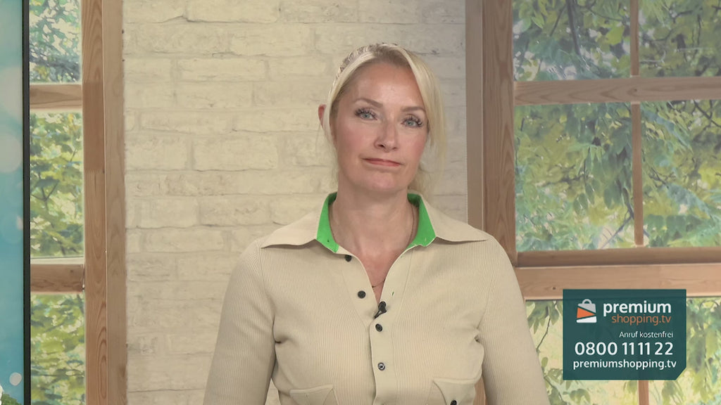 Video-Vorschaubild: Blonde Moderatorin in beige-grünem Oberteil vor einer Backsteinwand und einem Fenster, am linken Bildrand ein türkisfarbenes Produkt sichtbar, unten rechts das premiumshopping.tv-Logo mit Telefonnummer.