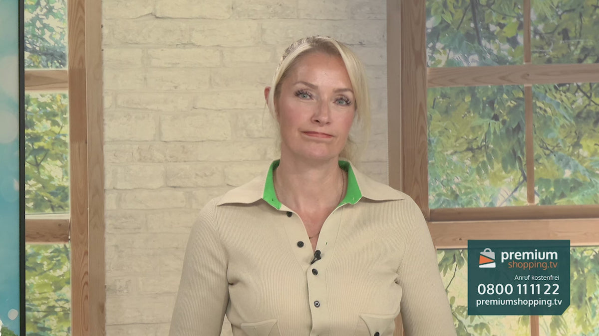 Video-Vorschaubild: Blonde Moderatorin in beige-grünem Oberteil vor einer Backsteinwand und einem Fenster, am linken Bildrand ein türkisfarbenes Produkt sichtbar, unten rechts das premiumshopping.tv-Logo mit Telefonnummer.